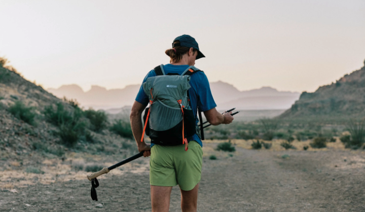 A hiker adjusts the tips of his trekking poles as he sets off down a dusty desert trail.