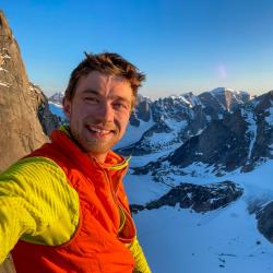 Miles smiles at the camera in front of a snowy mountain range