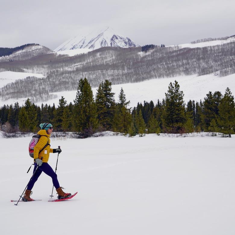 A woman walks across a snowy expanse on snowshoes