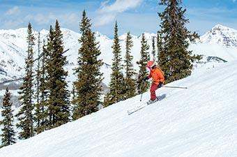 A skier turns down a slope on a sunny day in the mountains.