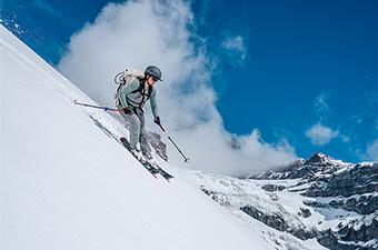 A skier rides down a snowy slope on a beautiful sunny day in the mountains.